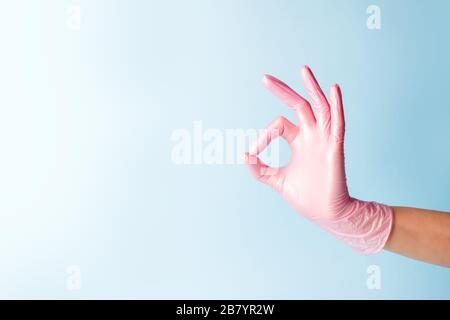 Weibliche Hand in der Kosmetikmedizin pinkfarbener Handschuh zeigt nach oben okay, ja, mit einem Handzeichen zur Seite, mit einem Studiofoto, einem Kopierraum und einem Banner für Ihren Flyer Stockfoto