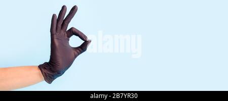 Weibliche Hand in der Kosmetologie-Medizin schwarzer Handschuh zeigt nach oben okay, ja, mit einem Handzeichen zur Seite, mit einem Studiofoto, einem Kopierraum und einem Banner für Ihren Flyer Stockfoto