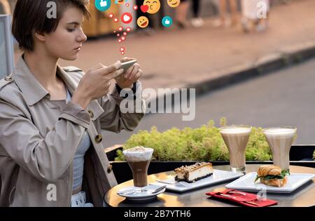 Mädchen Blogger sitzen am Café-Tisch machen Sie ein Lebensmittelfoto für instagram erhalten Sie "gefällt mir". Stockfoto