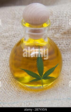Hanfprodukte - Hanfsaatöl in der Glasflasche mit dem Hanfblatt auf dem Hanfgewebe Stockfoto