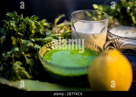 Haufen von Korianderblättern, Honig, Zitrone, Reis, Milch und Aloe Vera Gel Gesichtsmaske für alle Hauttypen und für natürliches Gesichtsleuchten auf einer schwarzen Holzsur Stockfoto