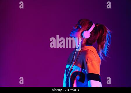 Happy Girl mit modischer Brille Kopfhörer hören Sie Musik im violetten Hintergrund. Stockfoto