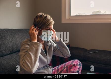 Frau in freiwilliger Einschließung mit Pyjamas, die chirurgische Masken zur Vorbeugung von Coronavirus-Kovid-Virus aufsetzen19. Sie arbeitet zu Hause mit dem Stockfoto