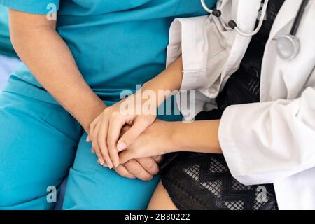 Schließen Sie den jungen weiblichen Arzt in einer einheitlichen Umarmung und lächeln Sie bei einem Besuch in der Krankenstation an die alte ältere Frau Stockfoto
