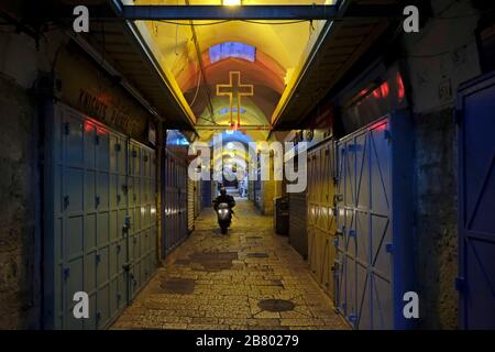 Ein Mann fährt mit dem Motorrad durch verschaltete Geschäfte in einer verlassenen Gasse im Christlichen Viertel in der Altstadt von Jerusalem. Israelische Tourismusindustrie schwer getroffen von Stornierungen inmitten Coronavirus Pandemie. Stockfoto