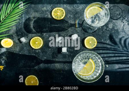 Wasser Zitrone detox. Reines kaltes Wasser mit Zitrone in Kristallgläsern auf dunklem Hintergrund in der sonnigen Sommersonne. Stockfoto