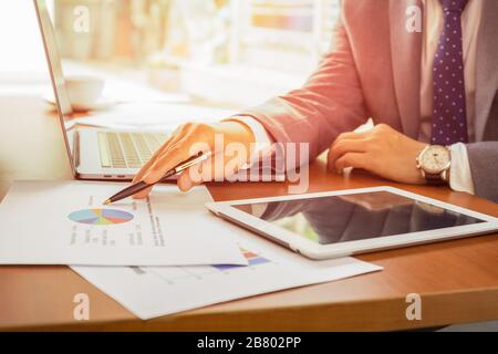 Unternehmer, die Stift halten und mit Laptops auf dem Tisch auf Finanzgrafiken zeigen. Stockfoto