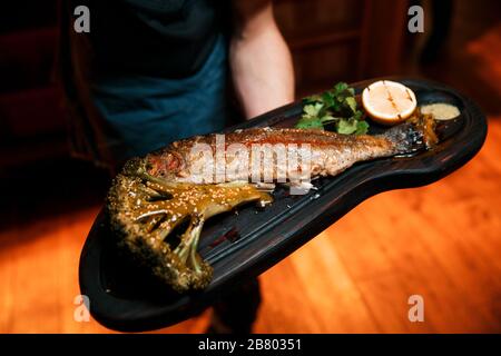 Gebackene Fische mit Zitrone liegen auf einem schwarzen Brett. Stockfoto