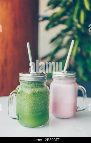 Gesunde Smoothie-Optionen in umweltfreundlichen Glasgefäßen mit Papierstraten in einem luxuriösen Fitnessbereich oder einem veganen Café. Trendige gedämpfte Tonbildung, Platz für Text Stockfoto
