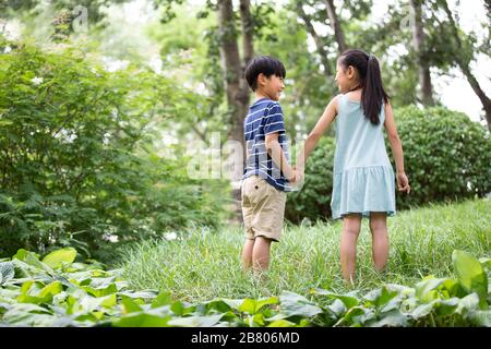 Zwei chinesische Kinder halten die Hände auf Gras Stockfoto