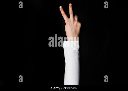 Mädchen Hand mit Friedenszeichen auf schwarzem Hintergrund Stockfoto