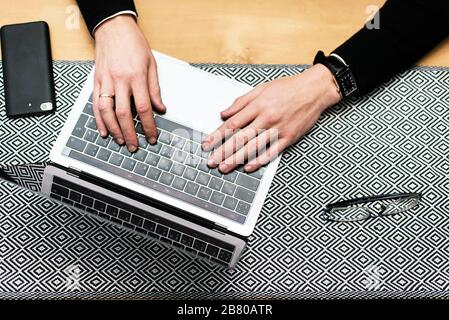 Nahaufnahme der Hände eines Mannes, der auf einer Laptop-Tastatur tippt. Zugeschnittenes Bild eines jungen Mannes, der in einem Café an seinem Laptop arbeitet. Stockfoto