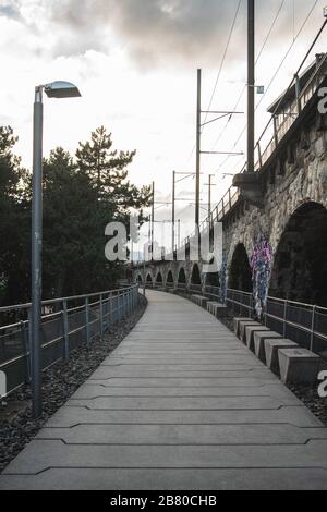 Langer gepflasterter Weg neben den Bögen eines Viadukts unter Ein wolkig Himmel Stockfoto