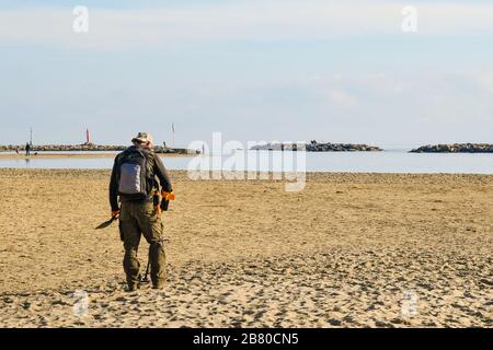 Ein Mann von hinten auf der Suche nach verborgenen schätzen mit einem Metalldetektor am Strand von Arma di Taggia, Imperia, Ligurien, Italien Stockfoto