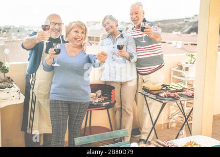 Fröhliche Senioren Freunde machen ein selfie-foto mit Smartphone beim Barbecue-Dinner im Terrassenhaus - reife Leute, die Spaß haben und Wein trinken - konzentrieren sich auf Stockfoto