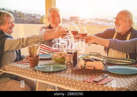 Gruppe glücklicher Senioren-Freunde jubelt beim Grillmenü auf der Terrasse im Freien - alte Menschen trinken Wein auf der Terrasse bbq Dinner - Hauptaugenmerk auf der linken Seite Stockfoto