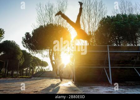 Freunde, die gleichzeitig Freestyle-Biking und Breakdancing durchführen - Break Dancer und Biker trainieren im Stadtpark - Extreme Sportkonzept - Stockfoto