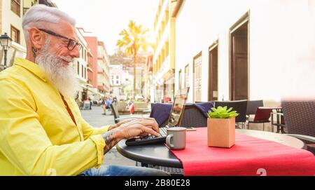 Fröhlicher Flusspferde mit Laptop in der Bar-Cafeteria im Freien - reifer modischer Mann mit Spaß beim Surfen im Internet und beim Kaffeetrinken - Technologie und Mode-li Stockfoto