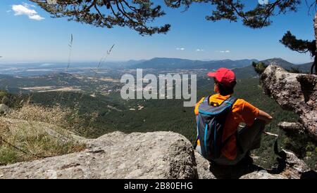 Junge Frau Wanderer, die auf dem Gipfel sitzen und die Talansicht betrachten, nachdem sie auf dem Weg GR-10 in Cercedilla wandern Stockfoto