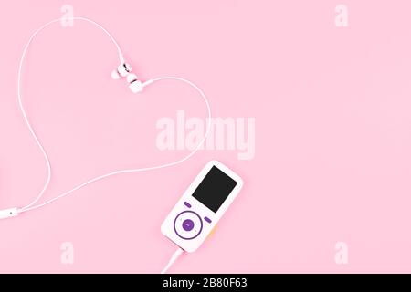 Weißer Musik-Player mit Ohrhörern, die sich in Form eines Herzens auf pastellrosa Hintergrund befinden. Konzept der Liebe zur Musik. Platz für Text, flaches Lay. Stockfoto