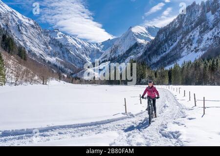 Schöne Seniorin, die an einem sonnigen Wintertag in den Allgauer alpen bei Oberstdorf, Bayern, mit ihrem elektrischen Mountainbike-Rad unterwegs ist Stockfoto