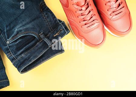 Pinkfarbene Turnschuhe und blaue Jeans auf pastellgelbem Hintergrund. Konzept von Sport Lifestyle und Casual Style. Platz für Text, flache Lage, Draufsicht. Stockfoto
