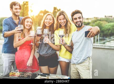 Fröhliche Freunde, die mit Smartphone auf der Grillparty fotografieren - junge Leute, die bbq-Abendessen im Freien kochen und Wein trinken - konzentrieren sich auf den richtigen Mann fa Stockfoto