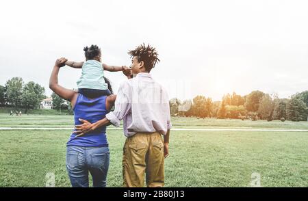 Glückliche schwarze Familie, die Spaß hat, im öffentlichen Park im Freien zu laufen - Eltern und ihre Tochter genießen zusammen Zeit an einem Wochenendtag - Liebe zärtliche Momente Stockfoto