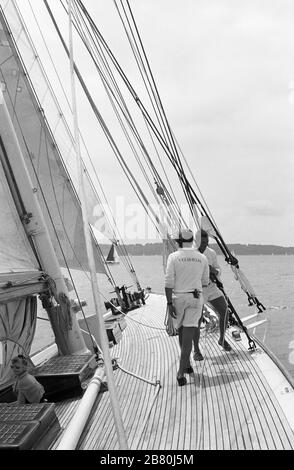 Crew-Mitglieder, die an Bord der Jacht "Velsheda" der J-Klasse an Deck arbeiten, nachdem sie das erste Mal wieder aufgestellt und im Sommer 1991 in Solent, Hampshire, England, Großbritannien, segelt haben. Foto des Schwarzweißfilms archivieren Stockfoto