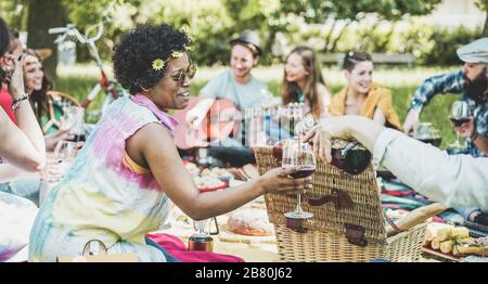 Eine Gruppe von Freunden, die Picknickmittagung machen und Wein im Freien trinken - junge Leute haben Spaß beim Essen und Entspannen - konzentrieren sich auf das gesicht afrikanischer Mädchen - out