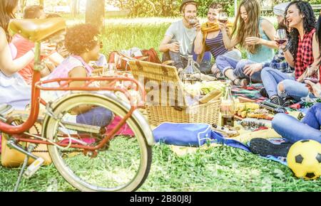 Vielfältige Kulturfreunde machen Picknick im Stadtpark im Freien - junge Trend-Leute trinken Wein und lachen draußen - konzentrieren sich auf den Mann mit Hut und zwei Gi Stockfoto