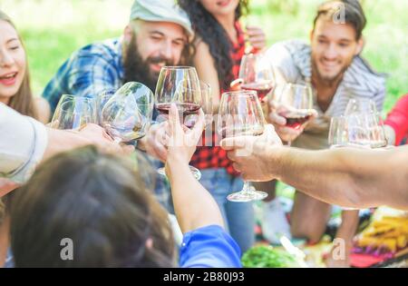 Fröhliche Freunde jubeln mit Weingläsern beim Picknick auf dem Stadtpark draußen - junge Trend-Leute, die Toast machen und gemeinsam lachen - konzentrieren sich auf Bottom ha Stockfoto