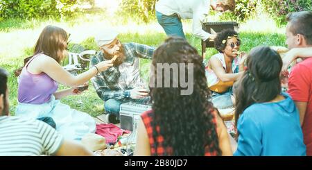 Eine Gruppe von Freunden, die im Stadtpark einen Picknickgrill machen - Junge Leute, die Spaß beim Musikspielen haben und sich auf der grillparty auf Gras entspannen - Main Stockfoto