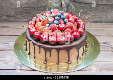 Schokoladenkuchen mit frischen Kirschen, Erdbeeren, Himbeeren und Blaubeeren auf Holzgrund Stockfoto