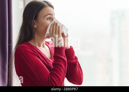 Kranke junge Frau mit Taschentuch. Weiblich mit Husten, Knall, Temperatur zu Hause in der Nähe des Fensters, Kopierraum Stockfoto