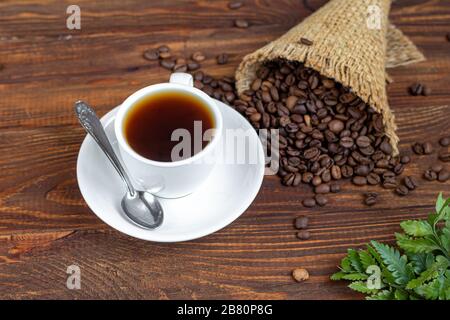 Weiße Tasse Kaffee. Auf Holzgrund. Kaffeebohnen sind über die gesamte Oberfläche verstreut. Kopierbereich Stockfoto