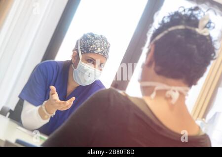 Ein weiblicher Arzt mit Schutzmaske spricht mit einem Patienten, der eine Maske trägt, um eine Infektion zu verhindern. Im Studio sitzen. Vertrauenskonzept für das Gesundheitswesen. Stockfoto