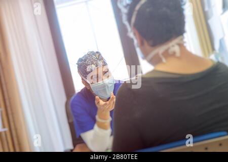 Ein weiblicher Arzt mit Schutzmaske spricht mit einem Patienten, der eine Maske trägt, um eine Infektion zu verhindern. Im Studio.Healthcare Trust-Konzept sitzen. Stockfoto