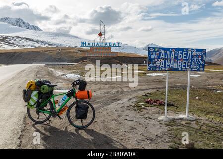 Provinz Chuy, Kirgisistan - 07. Oktober 2019: In der Nähe des Hinweisschildes Ala Bel Pass auf der Bishkek-Osh Autobahn M41 in Kyr steht ein Touristenrad mit Taschen Stockfoto