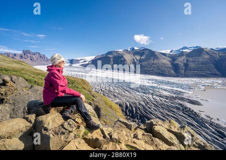 Aktive ältere Frau, die sich über dem Vatnajokull-Gletscher mit der Skaftafell-Gletscherzunge in Island ausruhte Stockfoto