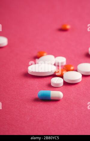 Pillen und Tabletten auf hellrotem Hintergrund, medizinisches Konzept für das Gesundheitswesen, Antibiotika und Heilmittel, Winkelansicht Stockfoto