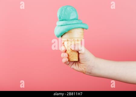 Eis in der Hand eines Kindes schmilzt auf einem rosafarbenen Hintergrund. Der Waffelkegel mit blauem Eis schmilzt. Stockfoto