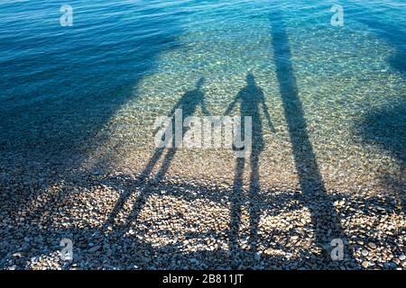 Ein liebevolles Paar an einem Strand, das Schatten im Meer erzeugt Stockfoto