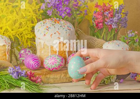 Osterei in der Hand auf einem Hintergrund von Ostern Dekoration und Blumen. Osterfrühstück Konzept. Schöne traditionelle Ostern Kuchen paska Stockfoto