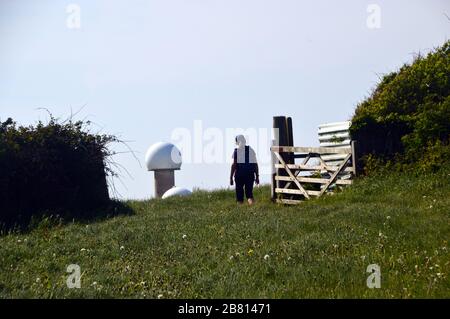 Woman Hiker, die durch Wooden Gate zu Air Traffic Control Radar Domes am Hartland Point auf dem South West Coastal Path, North Devon, England, gehen. Stockfoto