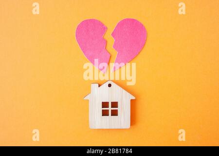 Scheidung, Aufteilung des Eigentums, Armut und kein Geldkonzept. Holzhaus mit gebrochenem Herzen auf hellorangefarbenem Hintergrund. Hypothek, Miete, Immobilienmakler Stockfoto
