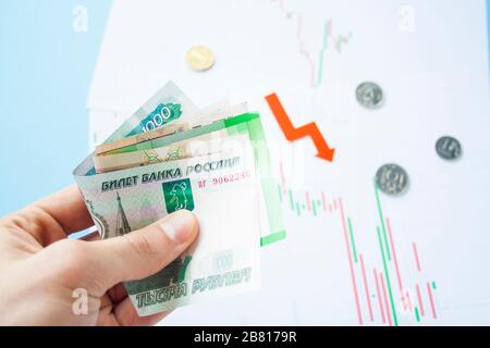 Männliche Hand, die Rubelrechnungen zum Wechselkurs des russischen Rubel und des roten Pfeils hält. Rubelabschreibung. Wechselkurs des Rubelfalls. Rubel zum Dollar Stockfoto