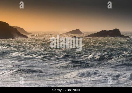 Die Sonne untergeht über Pentire Point East und zwei felsige Inseln namens Gull Rock und The Chick vor der Küste von Newuay in Cornwall. Stockfoto