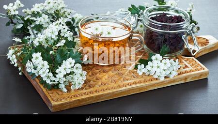 Kräuterdorntee aus Blumenknospen um blühende Zweige und ein Glas mit Beeren auf Holzschnittbrett, Nahaufnahme, Kopierraum, Herzgesundheit und h Stockfoto