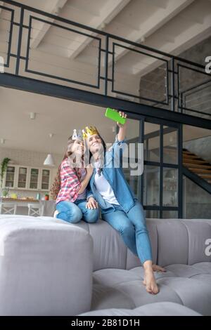 Mutter und Tochter tragen Kronen und machen selfie auf einem Smartphone Stockfoto